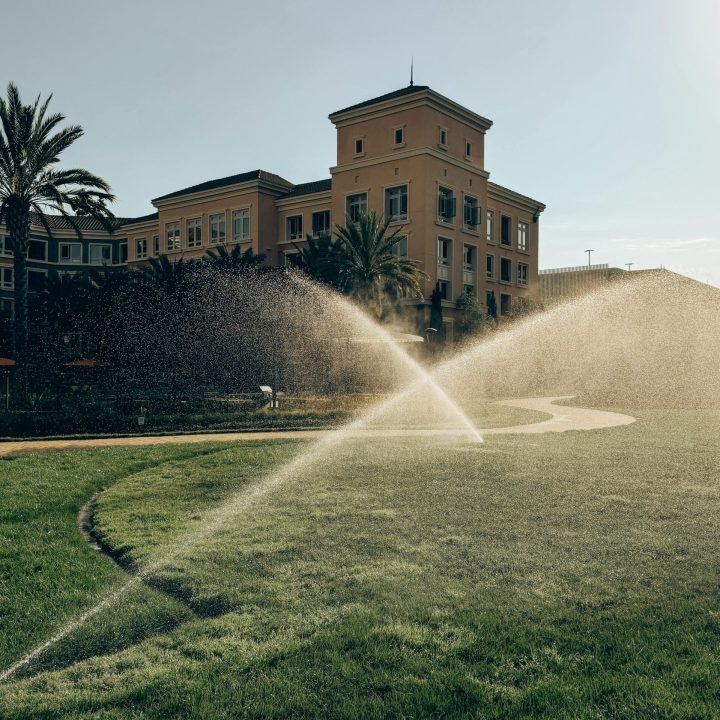 A charming building with a lush green lawn and sprinklers in action under a clear sky in Santa Clara, CA.